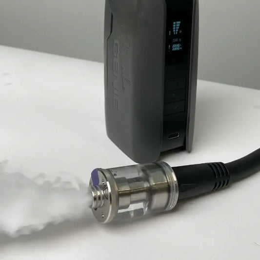A close-up of the PMI SmokeNINJA Extension Cable connected to a vaporizer, showing the mouthpiece and cable in focus as white vapor emits from the fog chamber, with device settings visible in the background.