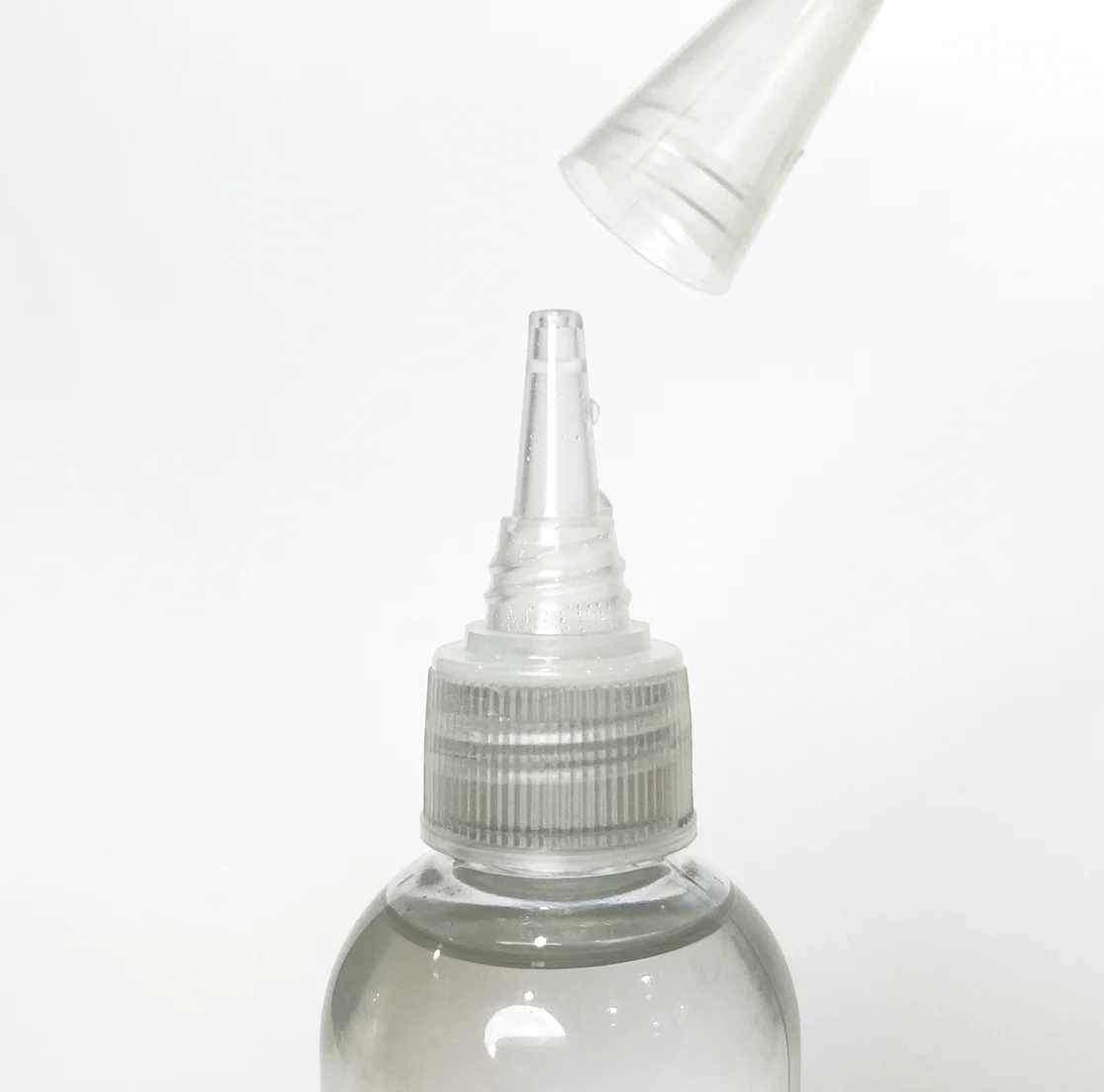 A close-up shows the PMI SmokeNINJA/GENIE Smoke Refill 100ml bottle with its transparent cap being lifted off the pointed nozzle, all set against a plain white background.