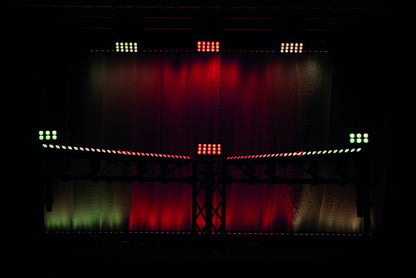 A dark stage is illuminated with red and green LED lights arranged in symmetrical patterns, creating a vibrant, colorful glow against a black and red backdrop. Featuring advanced stage lighting like the Showtec Cameleon Bar 15 Q6 Tour RGBWA-UV LED Bar from Showtec, the space is transformed into an immersive visual experience.