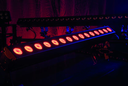 A row of vibrant red stage lights from the Showtec Cameleon Bar 15 Q6 Tour RGBWA-UV LED Bar illuminates a dark room with a purple backdrop, courtesy of Showtec, creating a dramatic and moody atmosphere.