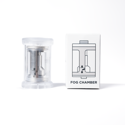 A stainless steel SmokeNINJA/GENIE Rep Shockproof Chamber (PMI_AC_CHAMB) by PMI sits in a clear plastic container beside a white box labeled Fog Chamber, with a line drawing of the smoke generator and an arrow illustration.