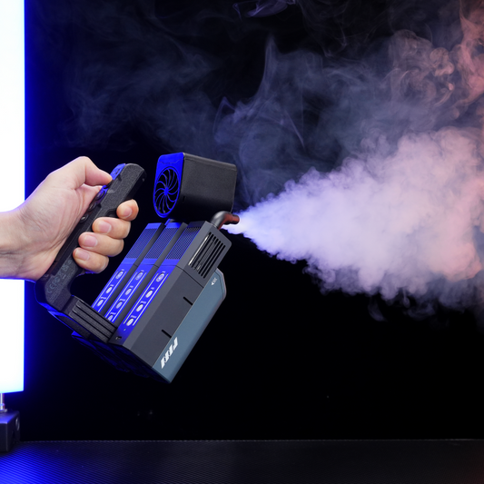 A hand holds the PMI SmokeNINJA Pro Trident Kit, emitting a thick stream of fog illuminated by blue lights against a dark background—ideal for adding cinematic effects to your video production.