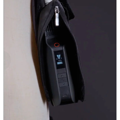A close-up of the PMI SmokeNINJA PRO/NINJA/GENIE PMI Smoke Vest (PMI_AC_SVEST), featuring a black electronic device with a small screen and buttons, partially zipped inside its black case, hanging from a white surface.