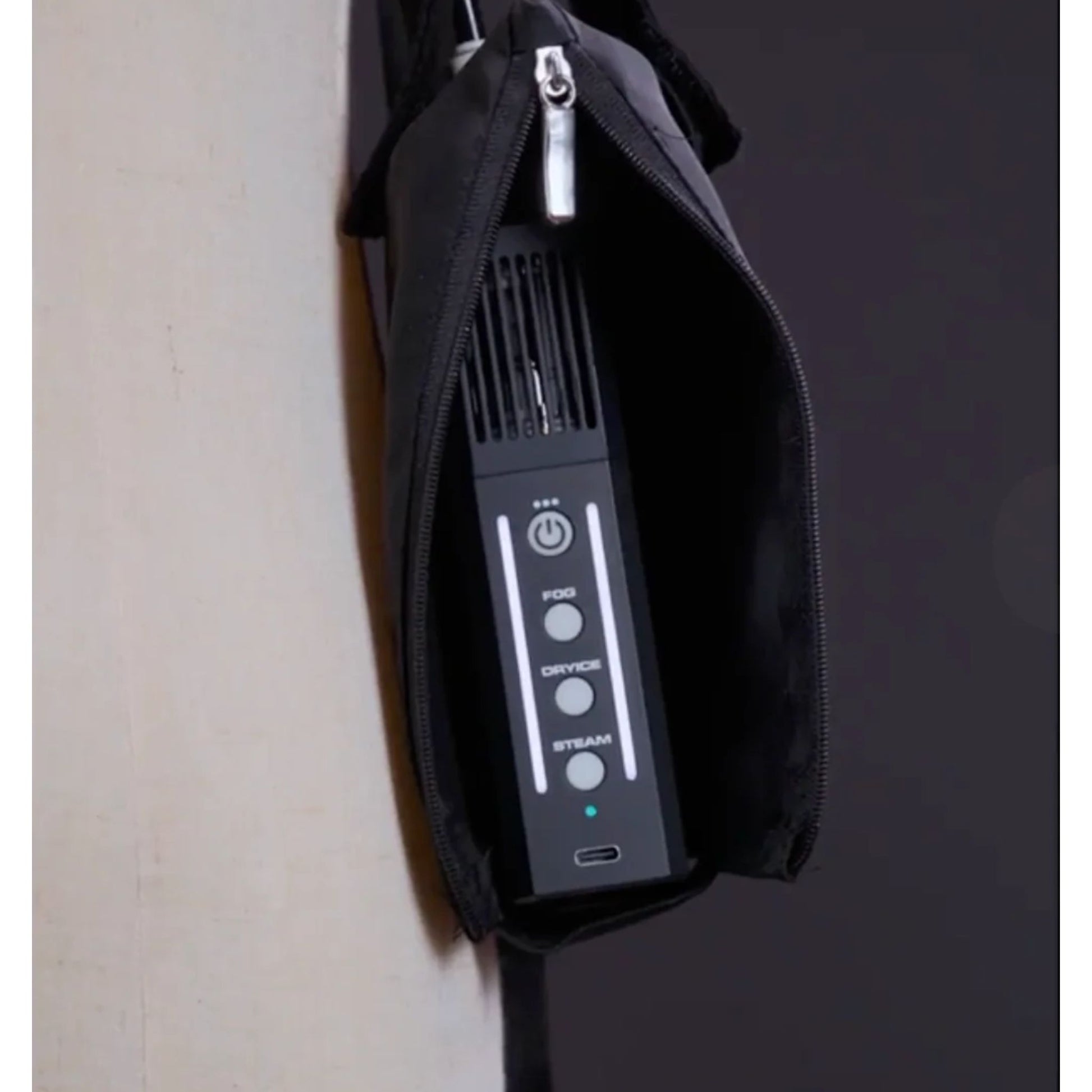 A close-up of a PMI SmokeNINJA PRO/NINJA/GENIE PMI Smoke Vest (PMI_AC_SVEST) in black, featuring buttons for Power, Fog, Cryo, and Steam. The electronic device stands upright inside a partially unzipped black case against a dark background.
