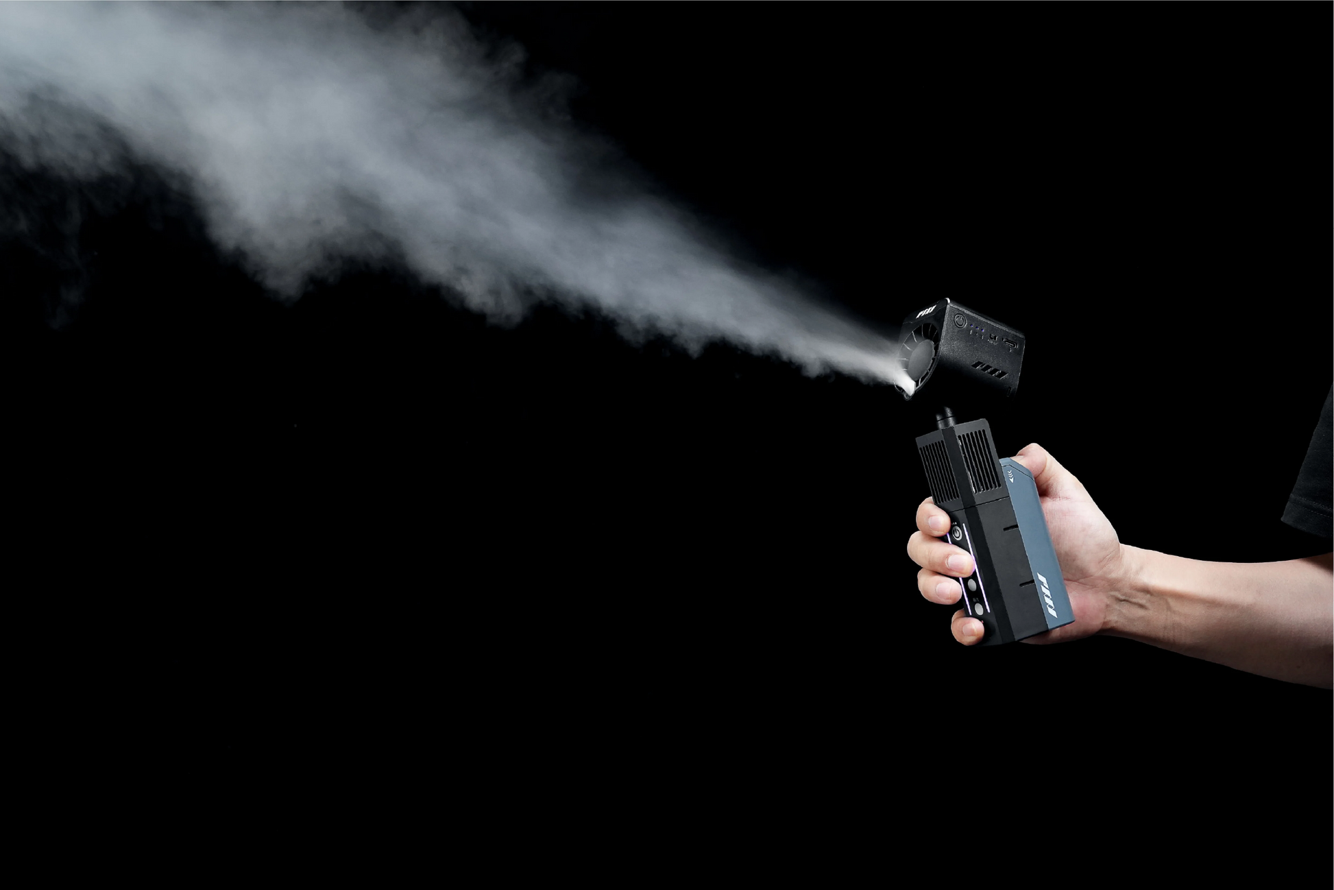 A hand holds the PMI SmokeNINJA Pro Trident Kit, a compact black device emitting white mist like a fog machine, set against a solid black background—ideal for creative video production.