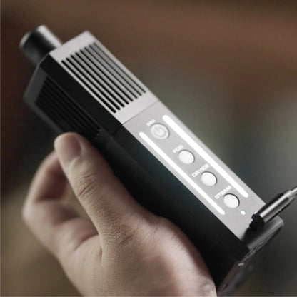 A hand holds the PMI SmokeNINJA Pro Trident Kit, a black device with vertical vents, labeled buttons, and glowing lights—indicating it's designed for cinematic fog effects in video production.