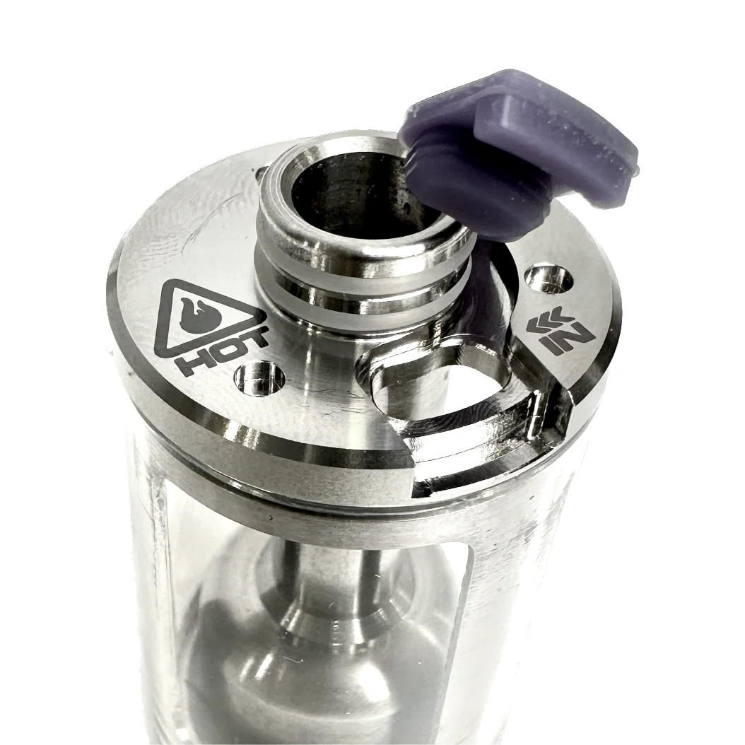 Close-up of the PMI SmokeNINJA/GENIE Rep Shockproof Chamber, featuring a transparent body, stainless steel details, a "HOT" warning symbol, and a purple silicone cap partially covering the top opening for optimal fog output.