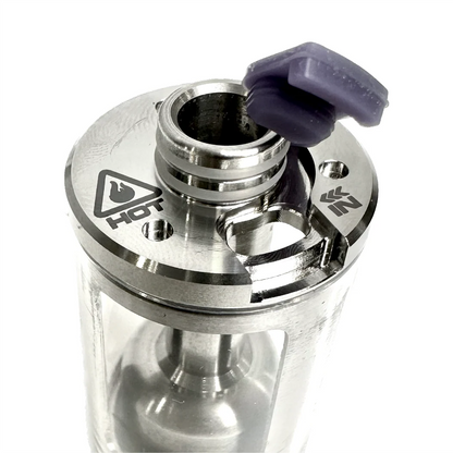 Close-up of the PMI SmokeNINJA/GENIE Rep Shockproof Chamber, featuring a transparent body, stainless steel details, a "HOT" warning symbol, and a purple silicone cap partially covering the top opening for optimal fog output.