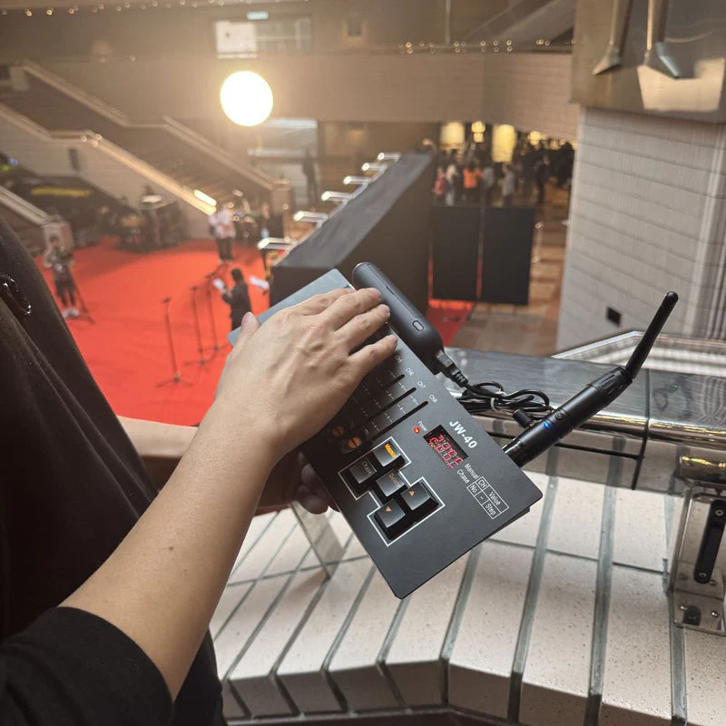 A person adjusts a portable video switcher above a venue, where the PMI SmokeNINJA PMI Wireless DMX Receiver coordinates the red carpet’s camera crew and lighting shimmering in the background.